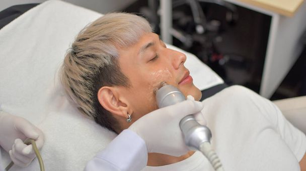 Yakışıklı bir Asyalı, modern tıbbi malzemeler kullanılarak güzellik kliniğinde yüz tazeleme ameliyatı oluyor. Standartlara göre sertifikalı güzellik uzmanları. - Fotoğraf, Görsel