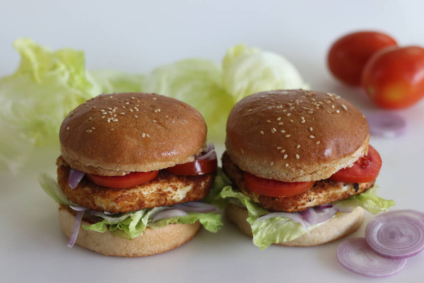 Homemade cottage cheese burger. Paneer or cottage cheese patties, tomatoes, onions and lettuce placed inside homemade burger buns. Shot on white background. - Photo, Image