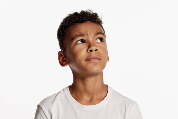 Dreaming. Cute african little boy wearing white t-shirt looks up in surprise isolated over white background. Kids emotions, goals, dreams, hope concept. Copy space for ad - Φωτογραφία, εικόνα