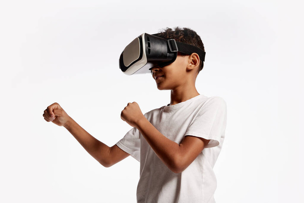 School age boy wearing casual style outfit enjoying 3D technology in virtual reality headset isolated on white background. Concept of cutting edge technology, video games, innovation and ad. - Foto, Bild