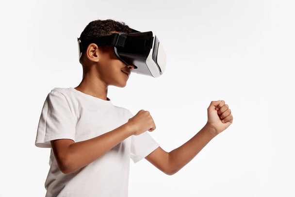 School age boy wearing casual style outfit enjoying 3D technology in virtual reality headset isolated on white background. Concept of cutting edge technology, video games, innovation and ad. - Foto, afbeelding