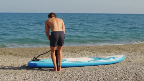 Jeune garçon gonfle la planche à souper en été sur la plage - Séquence, vidéo