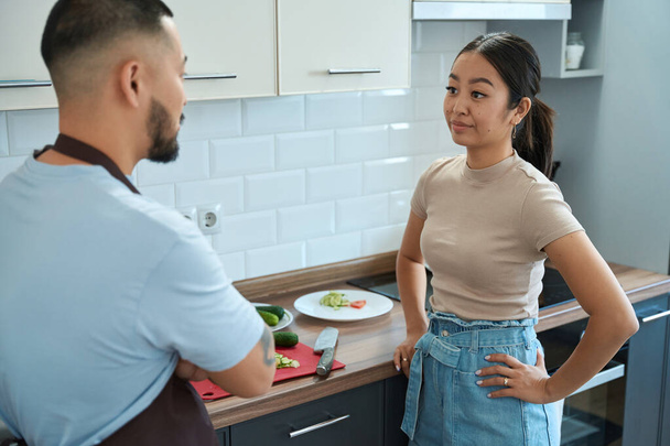 Young asian woman in denim shorts and a man with a tattoo are sorting things out in the kitchen - Foto, Imagen