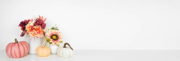 Herfst decor op een witte plank tegen een witte banner achtergrond. Pompoenen en bloemen in vazen met roze tinten vallen kleuren. Kopieerruimte. - Foto, afbeelding