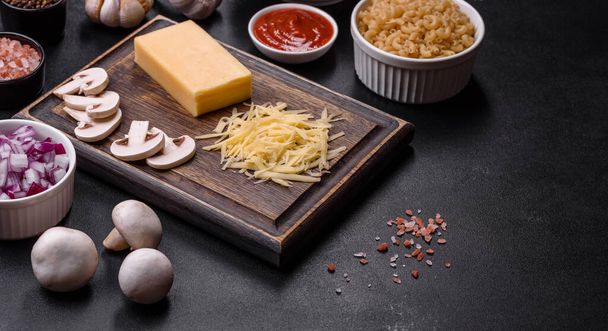 Сырая паста, грибы, лук, фарш, специи и травы, чтобы сделать вкусную пасту с томатным соусом на темном бетонном фоне - Фото, изображение
