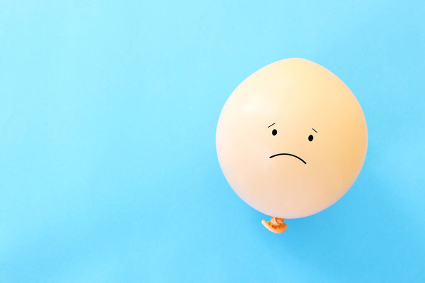 Top view image of balloon with sad face over blue background. Concept of emotions and sadness or stress - Foto, afbeelding