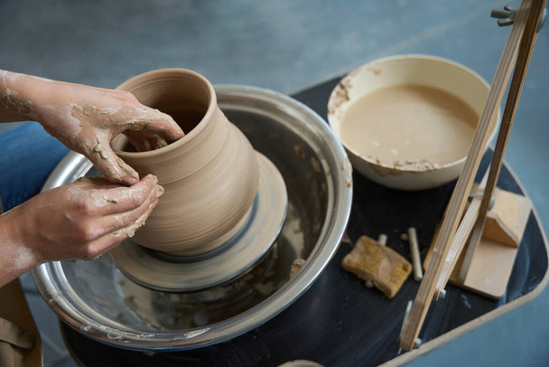 Pottenbakkershanden in het proces van het werken met een kleiproduct op een pottenbakkerswiel - Foto, afbeelding