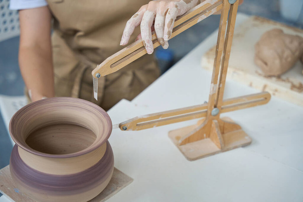 Close-up van het werk van een meester met een pottenbakkerskompas, zijn handen zijn bedekt met lichte klei - Foto, afbeelding