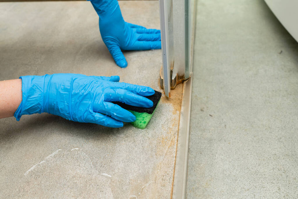 Vrouw in een blauwe handschoen reinigt een douchecabine van kalksteen - Foto, afbeelding