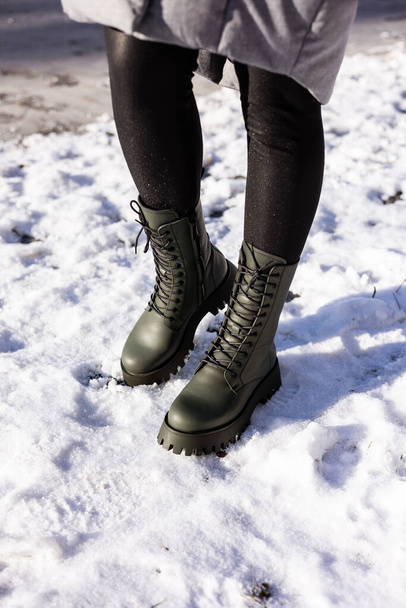 Close-up of female legs in green boots standing in the snow. Women's leather winter shoes - Photo, Image