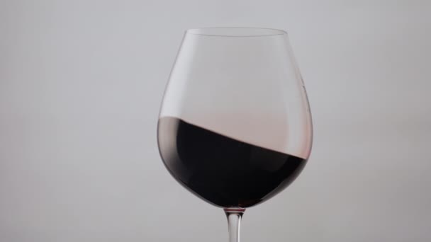 Mooie rode wijn golf in glazen beker op witte achtergrond close-up. Lekkere bordeaux alcoholische drank wervelend in transparante wijnglazen super slow motion. Kabeljauwoppervlak kabbelend in kristallen beker. - Video