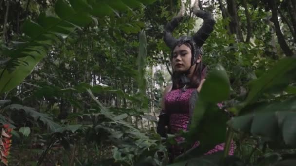 Mulher asiática em um traje de diabo escuro com um chifre preto na cabeça no festival de Halloween na floresta - Filmagem, Vídeo
