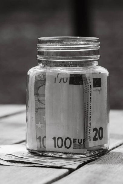 Samenstelling met het besparen van bankbiljetten in een glazen pot. Concept van beleggen en houden van geld, van dichtbij geïsoleerd. - Foto, afbeelding