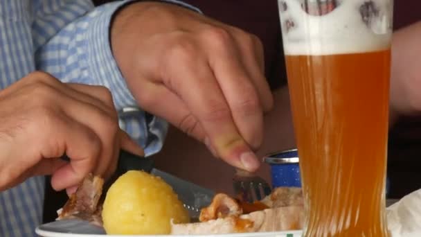 Палатки Октоберфест. Мужчина выпивает стакан пива и ест ножом и вилкой традиционную свиную наклу с капустой и жареной картошкой. Мюнхен, Германия. - Кадры, видео