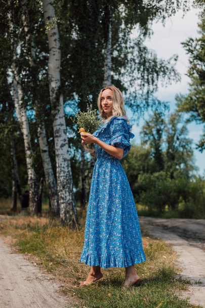 Une jeune blonde en robe longue aux fleurs sauvages se promène dans la forêt. Photo de haute qualité - Photo, image