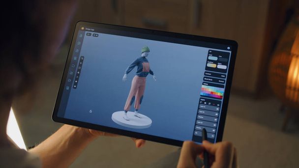 Αρσενικό 3D σχεδιαστής δημιουργία του σχεδιασμού των ρούχων σε 3D εφαρμογή μοντελοποίησης χρησιμοποιώντας το tablet υπολογιστή και ψηφιακό μολύβι, ενώ εργάζονται εξ αποστάσεως σε freelance έργο - Φωτογραφία, εικόνα