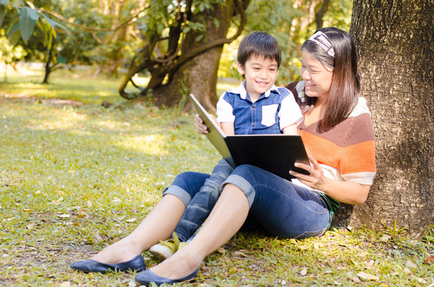 Mother and son read a book together in the park - Фото, зображення