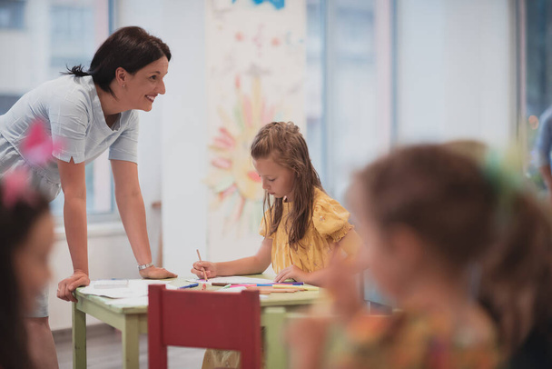 Creative kids during an art class in a daycare center or elementary school classroom drawing with a female teacher.  - Fotoğraf, Görsel