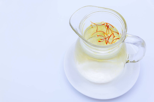 Saffron stamens in water in a jug on a white background. Saffron tea. Place for text. - Foto, Imagen