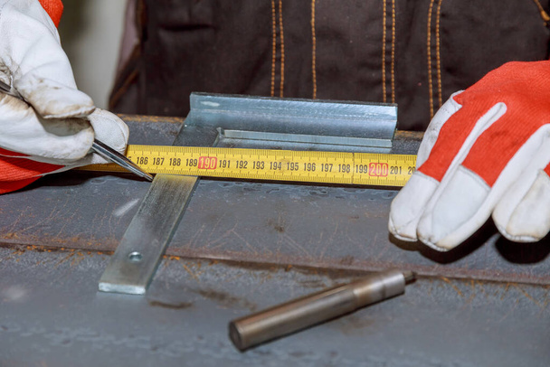 trabajador mide marcas en una superficie metálica para perforar agujeros. - Foto, imagen