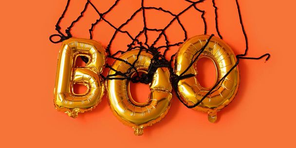 Palabra BOO hecha de globos y tela de araña sobre fondo naranja. Halloween celebración - Foto, Imagen