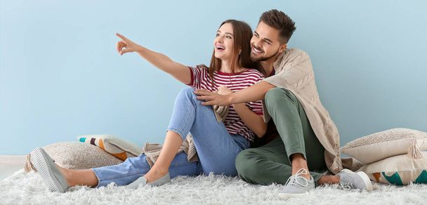 Porträt eines glücklichen jungen Paares, das auf dem Boden neben einer hellblauen Wand sitzt - Foto, Bild