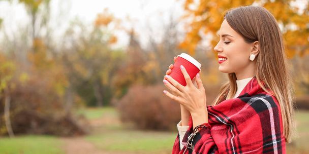 Стильна молода жінка п'є гарячу каву в парку в осінній день
 - Фото, зображення