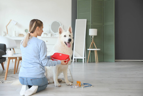 Woman with her white dog and first aid kit at home - Foto, afbeelding