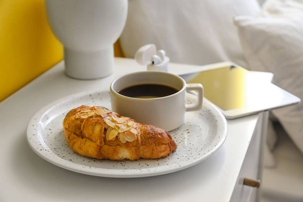 Plate with tasty croissant and cup of aromatic coffee on table in bedroom, closeup - Zdjęcie, obraz