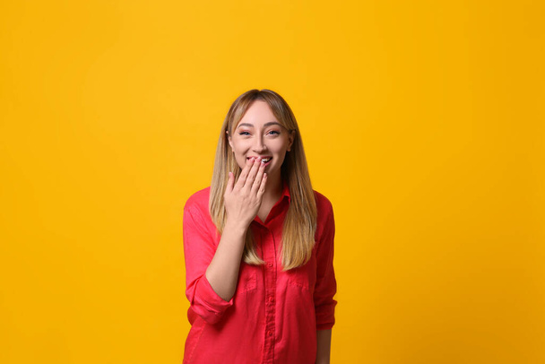 Beautiful young woman laughing on yellow background. Funny joke - Foto, afbeelding