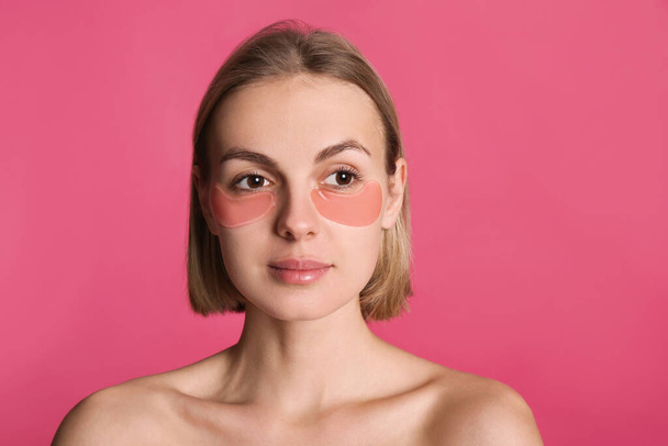Beautiful young woman with under eye patches on pink background - Foto, imagen