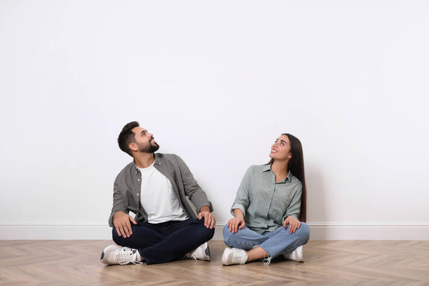Young couple sitting on floor near white wall indoors - Fotografie, Obrázek