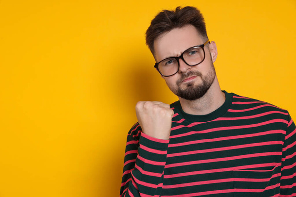 Aggressive man in striped sweatshirt and eyeglasses on yellow background, space for text - Фото, зображення