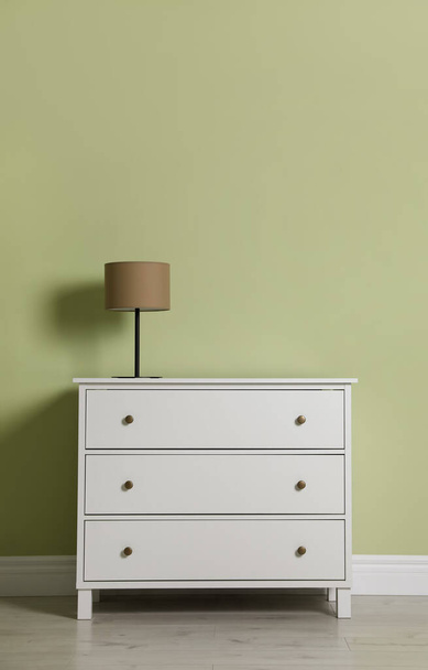 Modern white chest of drawers with lamp near light green wall indoors - Photo, Image