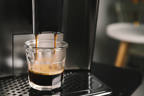 Espresso machine pouring coffee into glass against blurred background, closeup. Space for text - Fotoğraf, Görsel
