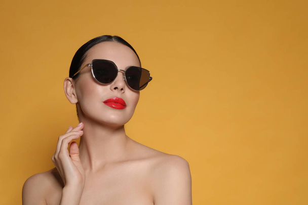 Attractive woman in fashionable sunglasses against orange background. Space for text - Φωτογραφία, εικόνα