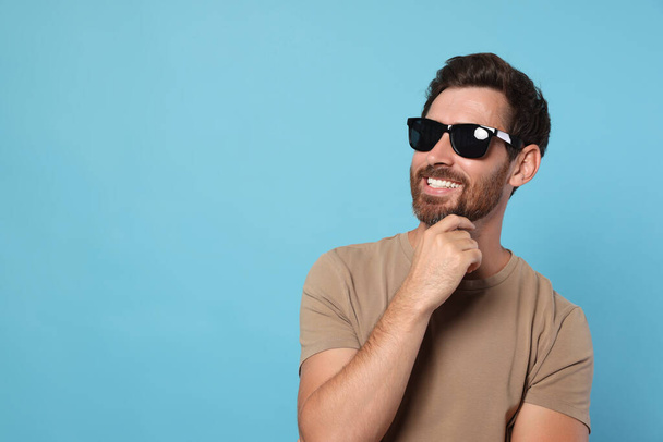 Portrait of smiling bearded man with stylish sunglasses on light blue background. Space for text - Photo, image