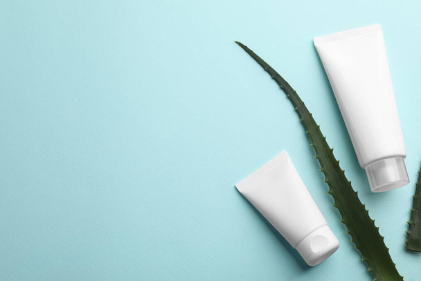 Tubes of hand cream and aloe on turquoise background, flat lay. Space for text - 写真・画像