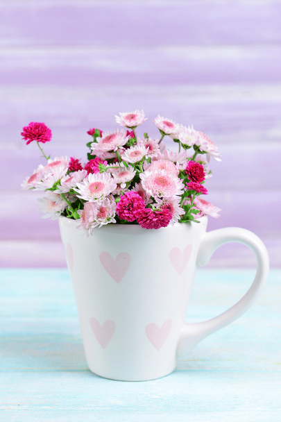 Beautiful flowers in cup on table on purple background - Photo, Image