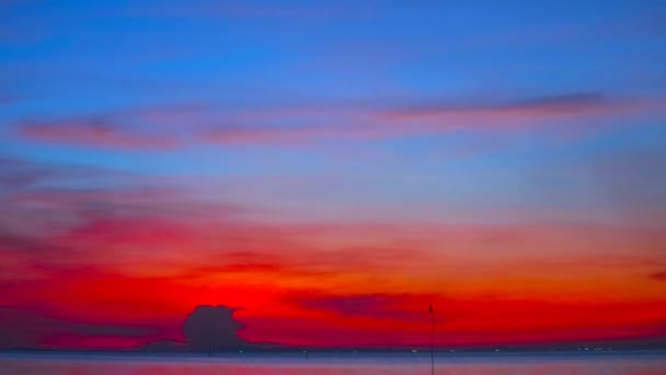 rozmyty zachód słońca czerwony błękitne niebo z ciemną chmurą nad morzem i flaga sylwetki na bambus - Materiał filmowy, wideo