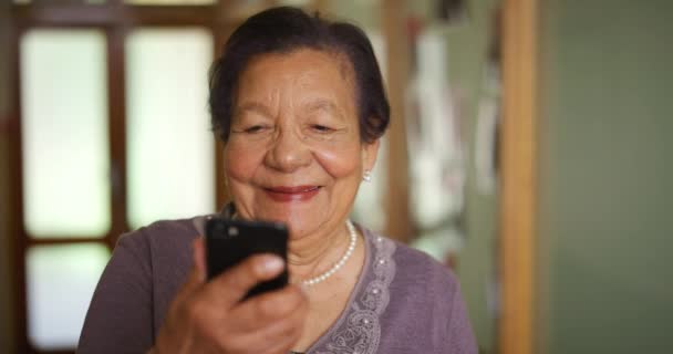 Senior, sonrisa y teléfono de una anciana de China leyendo un texto en un móvil en casa. Mujer asiática feliz utilizando la tecnología mirando a la web, Internet o un contenido de redes sociales en línea con una sonrisa. - Imágenes, Vídeo