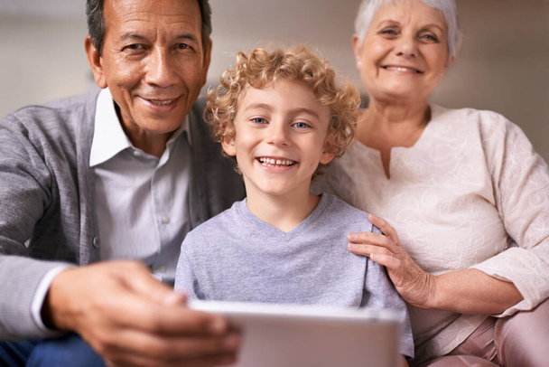 Wer braucht schon technische Unterstützung, wenn man Enkel hat. Ein kleiner Junge hält ein Tablet in der Hand, während er bei seinen Großeltern sitzt - Foto, Bild