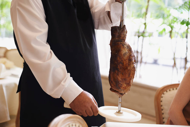 That looks delicious. Cropped image of a male waiter holding a large piece of meat on a stake - Photo, Image