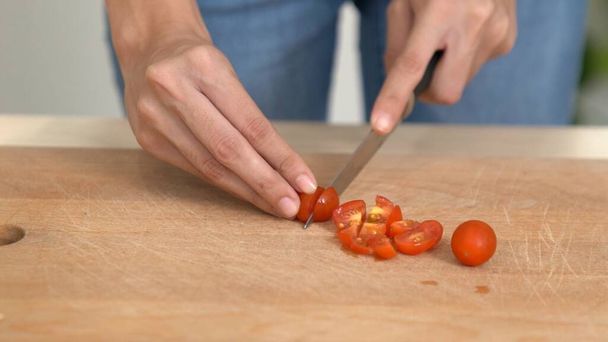 Κοντά τα χέρια κρατώντας ένα μαχαίρι ετοιμάζοντας ένα ικανοποιημένο γεύμα. Τομάτες κομμένες και άλλα λαχανικά στο γυάλινο πιάτο. - Φωτογραφία, εικόνα
