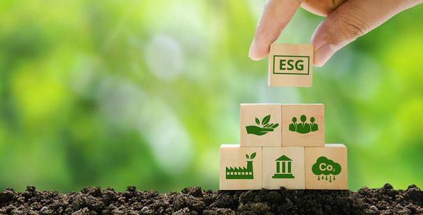 Koncepcje ESG w zakresie środowiska, społeczeństwa i zarządzania zrównoważony rozwój przedsiębiorstw Ręczne trzymanie drewnianego sześcianu ze skrótem ESG na zielonym tle. - Zdjęcie, obraz