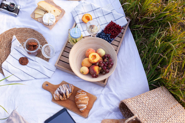 White blanket with fruits and pastries, lemonade, cookies, cheese and straw bag with baguette. Concept of having picnic in a city park during summer holidays or weekends. Copy space. - Foto, Bild