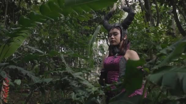 アジアの女性は暗い悪魔の衣装を着て、黒い角を頭にしてハロウィーンの祭りで森の中で - 映像、動画