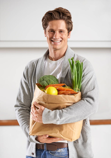 Vain luomua minulle. Nuori mies keittiössä pitäen ruskeaa paperipussia täynnä vihanneksia. - Valokuva, kuva