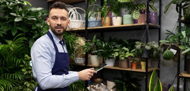 joven empresario florista con una tableta en sus manos en el fondo de una floristería. - Foto, Imagen
