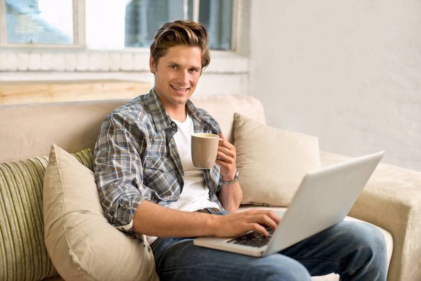 A vezeték nélküli technológiának megvannak az előnyei. Egy jóképű fiatalember használja otthon a laptopját. - Fotó, kép